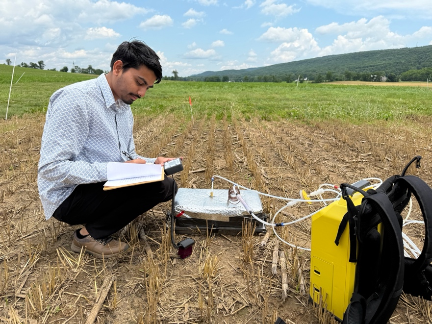 Saurab recording measurements beside a Gasmet gas analyzer in a field plot